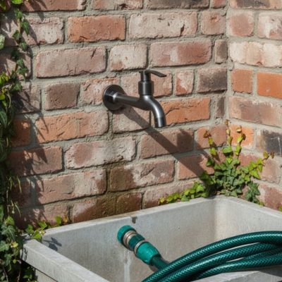 robinet extérieur sur mur en brique rouge surmonte fontaine avec tuyau arrosage dedans